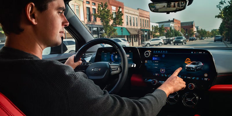 Driver interacting with the Chevrolet infotainment system displaying a vehicle safety-assistance feature with a collision warning icon highlighted above the vehicle graphic.