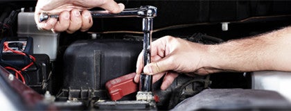 Two hands using a socket wrench to work on a car engine.